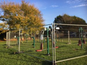 Outdoor gym equipment surrounded by fencing in the Autumn sun